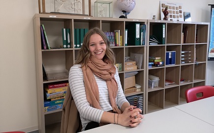 Die 20-Jährige Lina Kittner sitzt lächelnd an einem Tisch in einem lernbüro der DPFA Regenbogen Schulen Rabenau.
